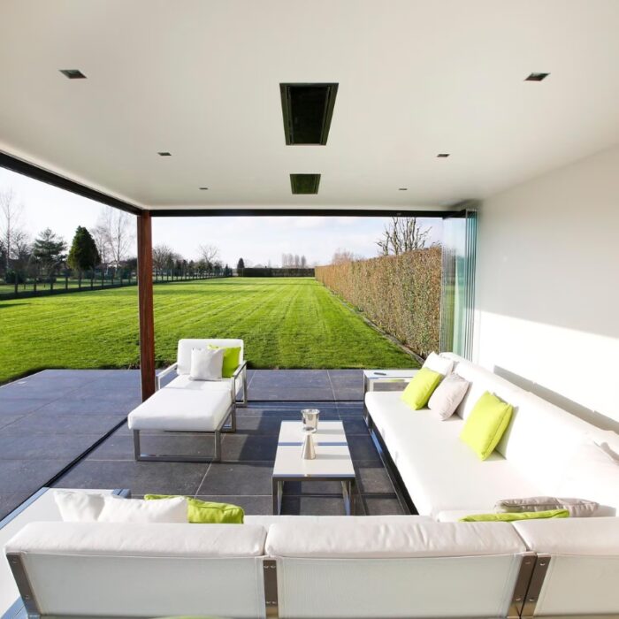 Modern outdoor living space with white furniture and green accents, showcasing a spacious lawn and hedges in the background.