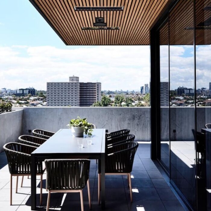 Modern outdoor dining area with a long table and stylish chairs, overlooking a city skyline under a clear blue sky.