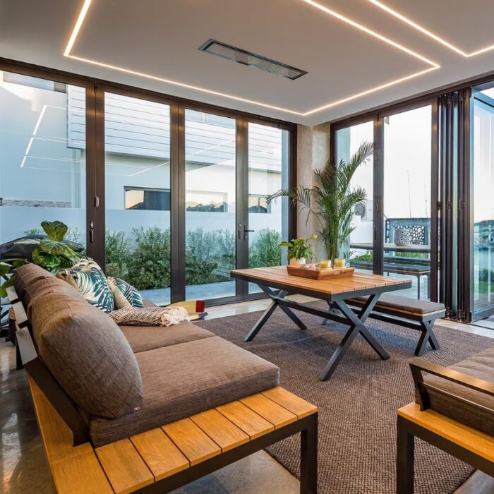 Modern living room with large glass doors, comfortable gray sofa, wooden coffee table, and indoor plants, featuring stylish decor and natural light.