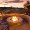 Cozy outdoor fire pit with stone seating under a colorful sunset, surrounded by natural landscaping and a serene atmosphere. Perfect for gatherings and relaxation.