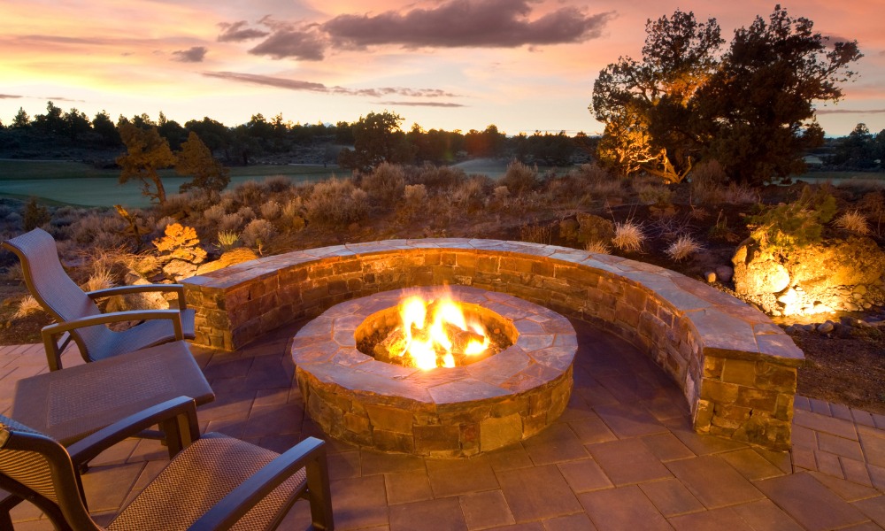Cozy outdoor fire pit with stone seating under a colorful sunset, surrounded by natural landscaping and a serene atmosphere. Perfect for gatherings and relaxation.