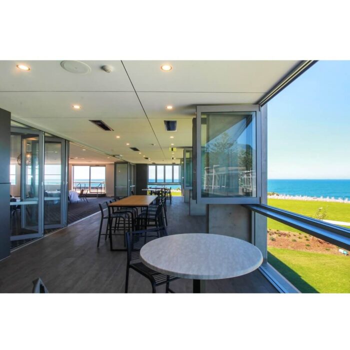 Modern interior of a beachfront restaurant featuring large windows and tables, with a view of the ocean and green lawn outside.