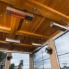 Ceiling view featuring infrared heaters and ceiling fans in a modern indoor space with wooden beams and large windows.