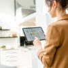 Woman using a tablet to control smart home devices in a modern kitchen setting.