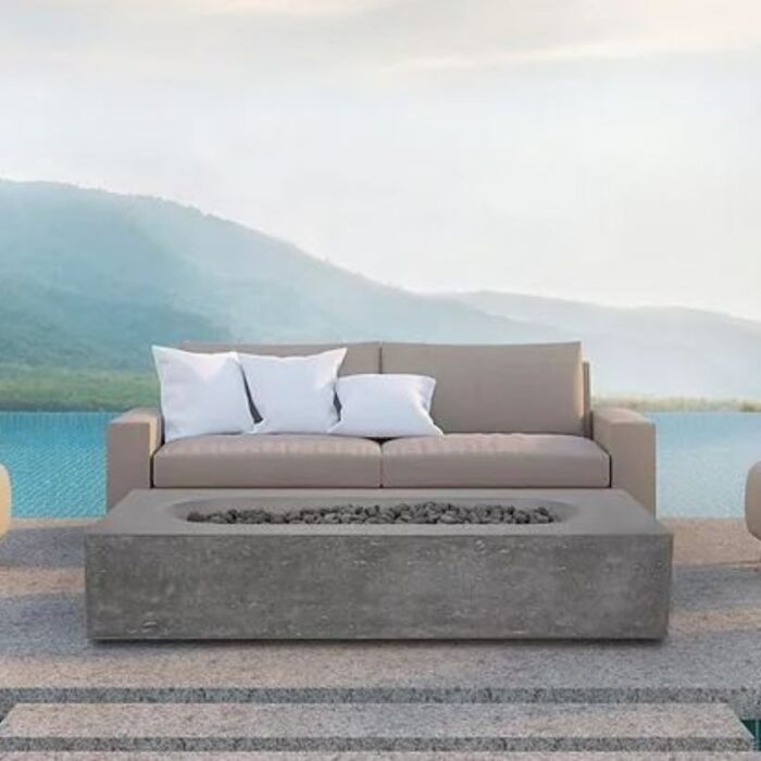 Modern outdoor seating area featuring a beige sofa with white pillows and a concrete coffee table, set against a serene lake and mountain backdrop.