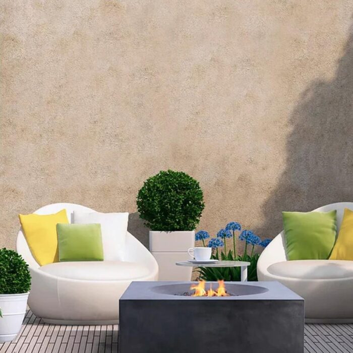 Modern outdoor seating area with white chairs, colorful cushions, potted plants, and a fire pit, set against a textured wall.