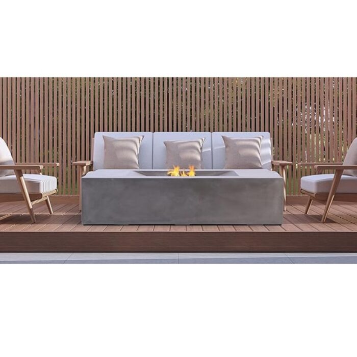 Modern outdoor seating area featuring a stylish fire pit table, comfortable white sofa with decorative pillows, and wooden deck surrounded by a slatted privacy fence.