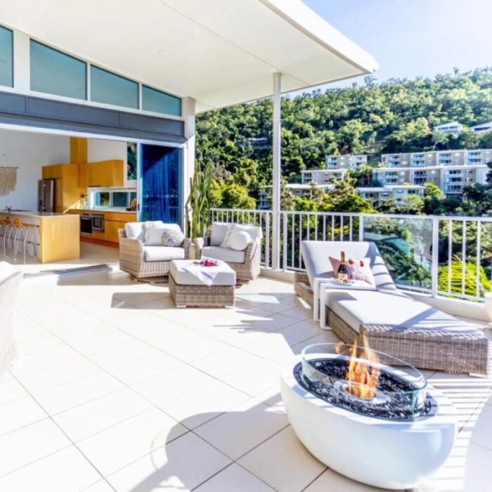 Modern outdoor patio with comfortable seating, a fire pit, and scenic views of lush greenery and nearby buildings. Ideal for relaxation and entertaining.
