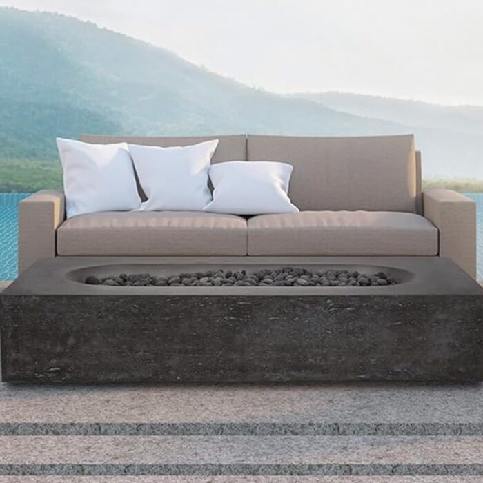 Outdoor seating area featuring a modern beige sofa with white cushions and a dark stone coffee table with a built-in fire pit, set against a scenic backdrop of mountains and a pool.