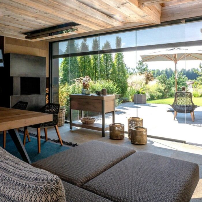 Stylish modern living room with large glass doors opening to a lush outdoor garden, featuring a wooden table, comfortable seating, and decorative elements.