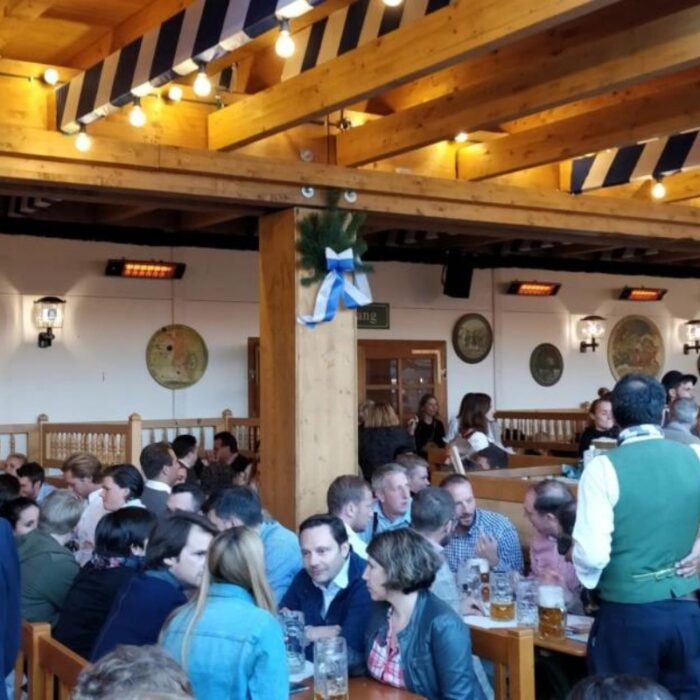 Busy beer hall with wooden beams and festive decorations, featuring patrons enjoying drinks and conversation.