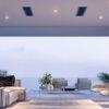 Modern coastal living room with a view, featuring a light-colored sofa, a glass coffee table, and stylish chairs, surrounded by large windows and tropical plants.