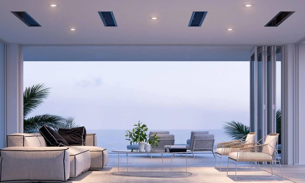 Modern coastal living room with a view, featuring a light-colored sofa, a glass coffee table, and stylish chairs, surrounded by large windows and tropical plants.