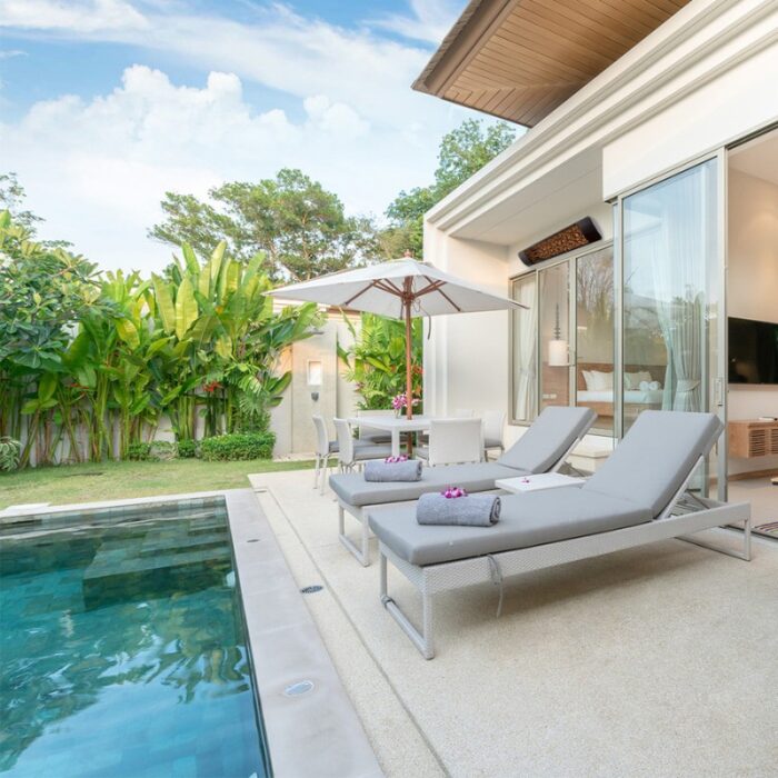 Modern villa patio with pool, sun loungers, and dining area surrounded by lush greenery. Ideal for relaxation and outdoor living.