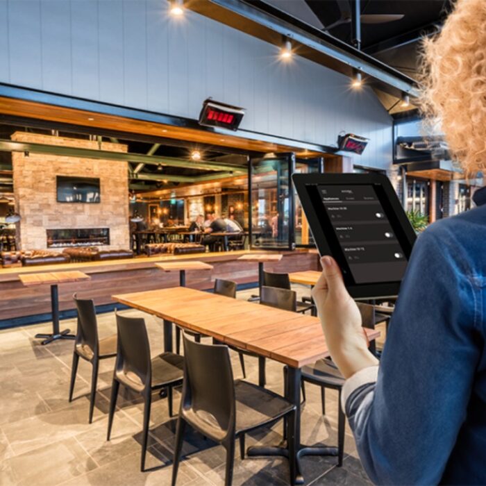 Person using a tablet to manage settings in a modern restaurant with a stylish interior and wooden tables.