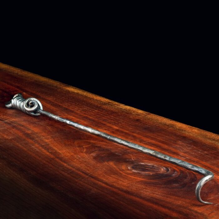 Handcrafted metal hook tool resting on a polished wooden surface, showcasing intricate spiral detailing at one end.