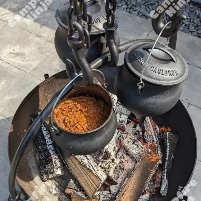 Cooking beans in a cast iron cauldron over an open fire, surrounded by glowing embers and wooden logs.