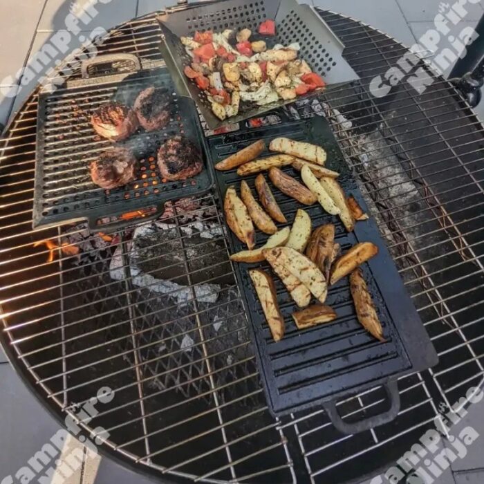 Close-up of a barbecue grill featuring grilled steaks, seasoned potato wedges, and mixed vegetables, showcasing a delicious outdoor cooking setup.