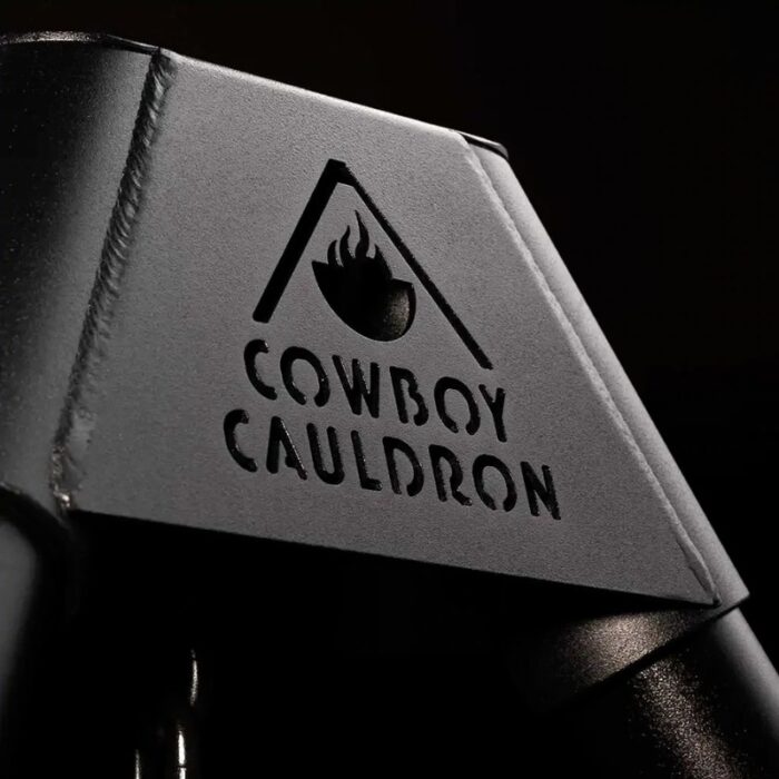 Cowboy Cauldron logo embossed on a black surface, showcasing a minimalist design with an upward triangle and flame graphic.