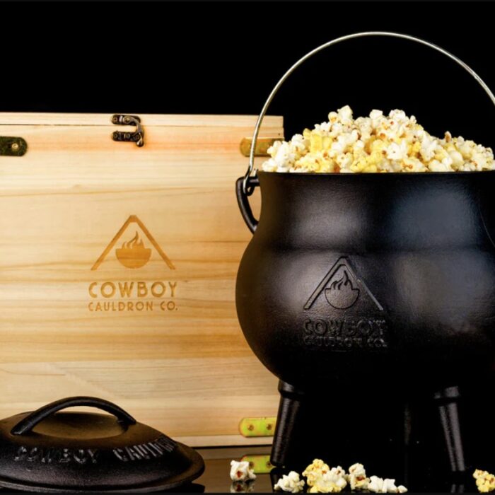 Cast iron cauldron filled with popcorn, accompanied by a wooden box featuring the Cowboy Cauldron Co. logo.