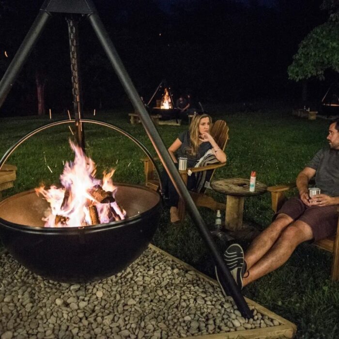 Cozy evening by a fire pit with two people relaxing in Adirondack chairs, surrounded by a grassy outdoor setting.