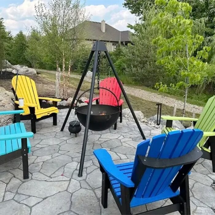 Colorful Adirondack chairs arranged around a central fire pit on a stone patio, surrounded by greenery and a residential home in the background.