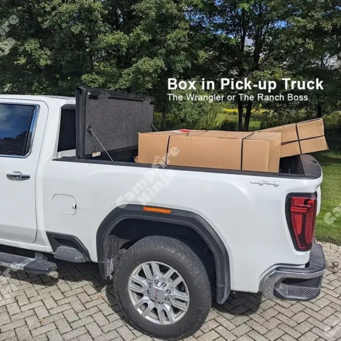 White pickup truck with a closed toolbox in the bed carrying several boxes, parked on a paved area surrounded by trees.