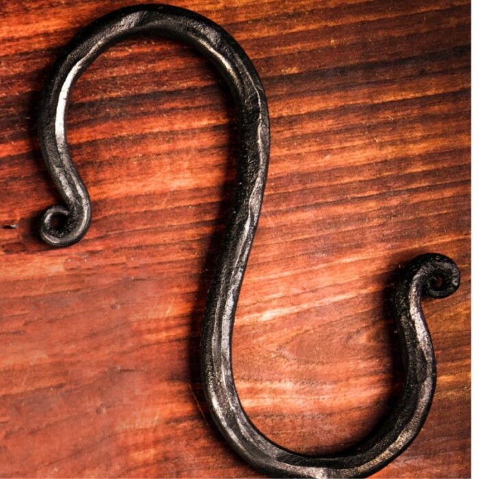 Iron hook with a decorative twisted design resting on a wooden surface.