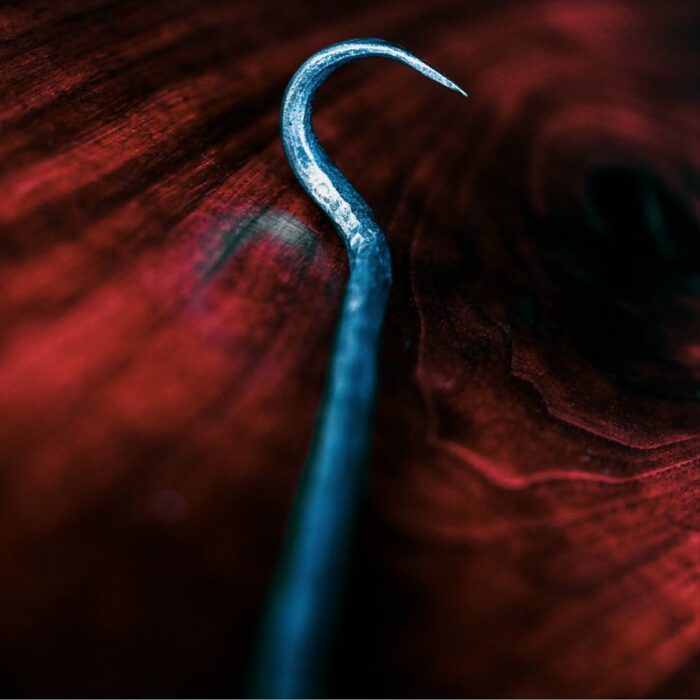 Close-up of a metal hook resting on a dark wooden surface, showcasing its curved end and shiny texture.