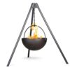 Black cauldron hanging from a metal tripod with flames inside, designed for outdoor cooking and gatherings.