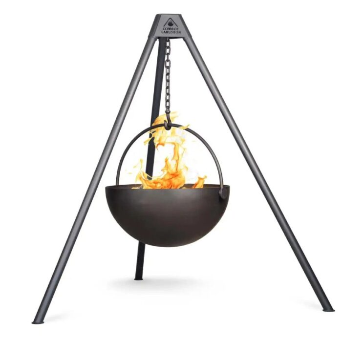 Black cauldron hanging from a metal tripod with flames inside, designed for outdoor cooking and gatherings.
