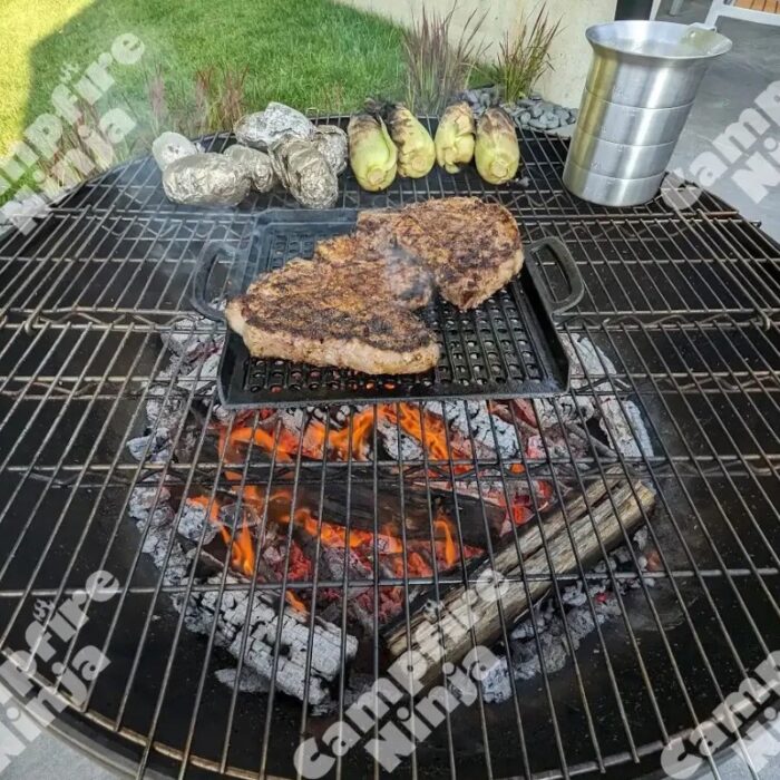 Grilled steaks on a barbecue with smoky flames, surrounded by baked potatoes and corn on the cob, showcasing a delicious outdoor cooking scene.