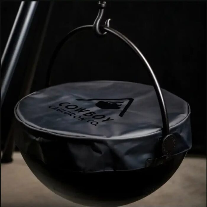 Black cauldron with a lid, hanging from a hook, featuring the logo of Cowboy Cauldron Co. against a dark background.