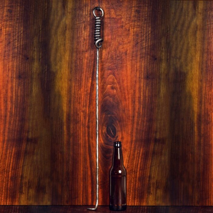 Iron tool with a coiled top standing next to a brown glass bottle on a wooden background.