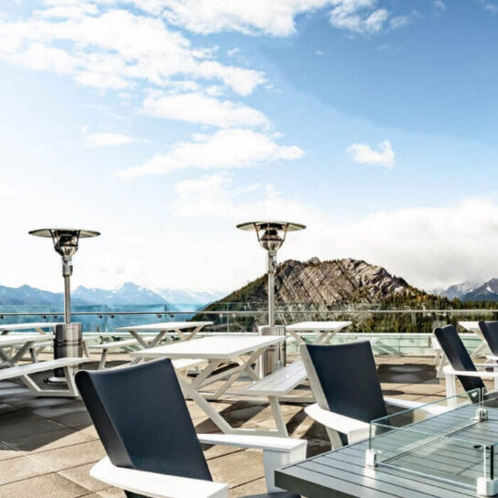 Outdoor terrace with modern seating and patio heaters, overlooking a mountain landscape under a clear blue sky.