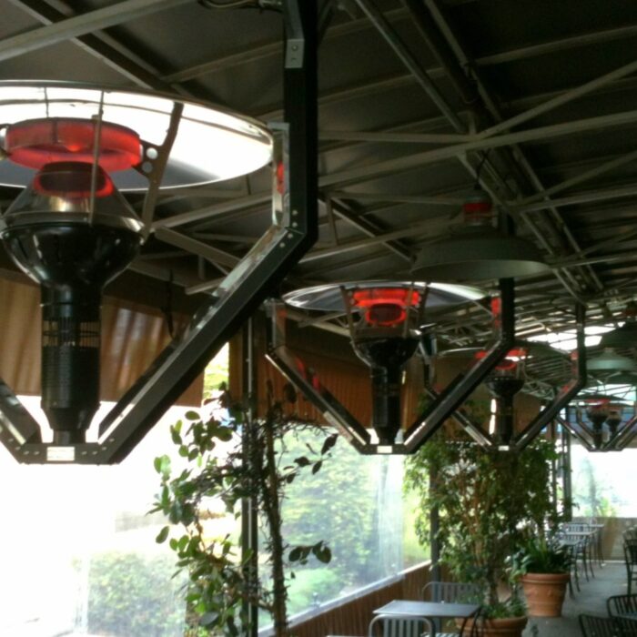 Outdoor patio with overhead infrared heaters providing warmth, surrounded by greenery and seating areas.