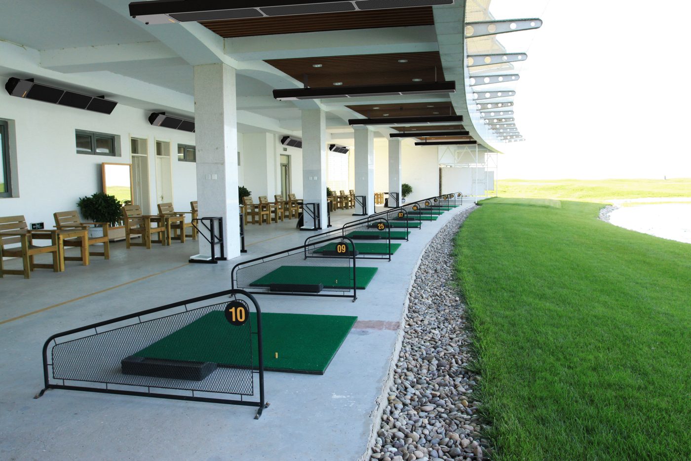 Row of phantomSchwank tube heaters above numbered golf driving range tee bays